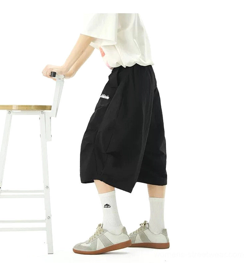 Side view of black oversized balloon jogger shorts showing the cropped mid-calf length, wide lantern-shaped legs, elastic drawstring waist, and relaxed urban silhouette