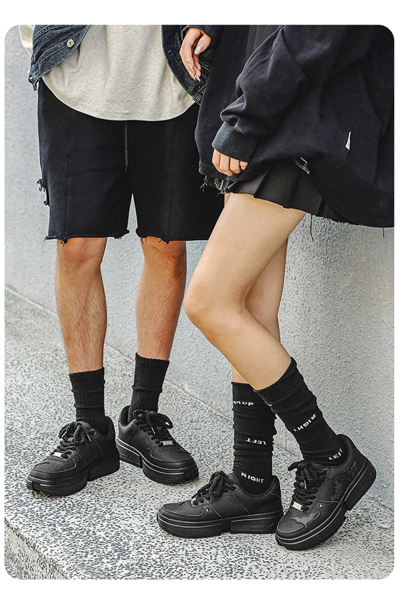 Couple wearing matching black bat crest platform sneakers with black crew socks and coordinated dark streetwear outfits