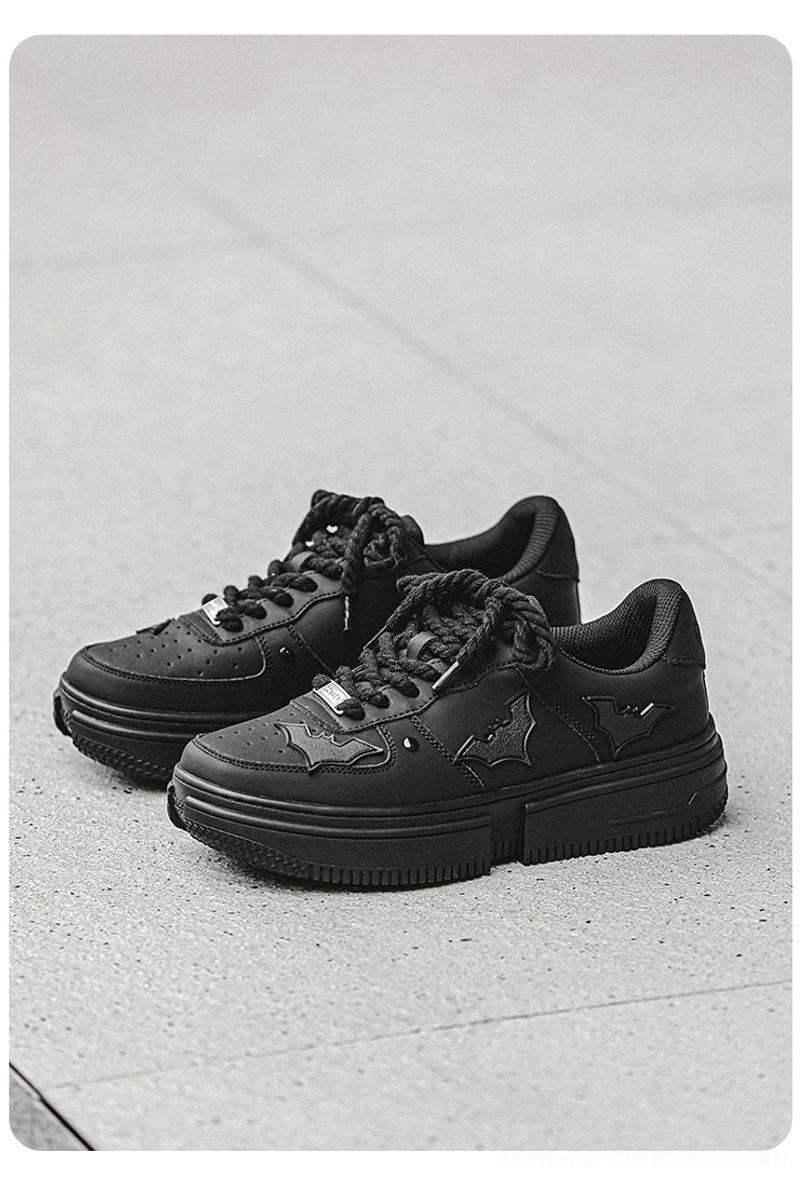 Front three-quarter product view of black bat crest platform sneakers with metal lace lock and matte black platform outsole