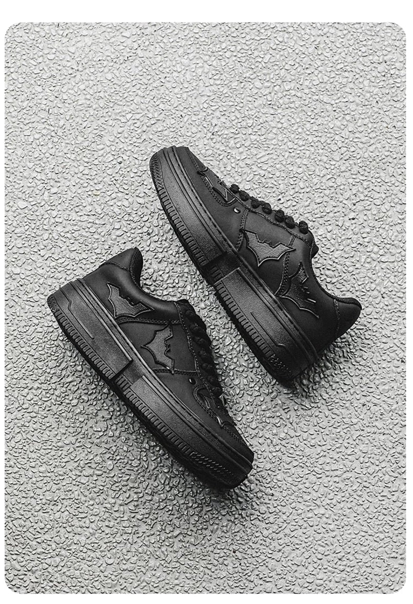 Top-down flat lay of black bat crest platform sneakers with embossed wing logos and chunky round toe streetwear design