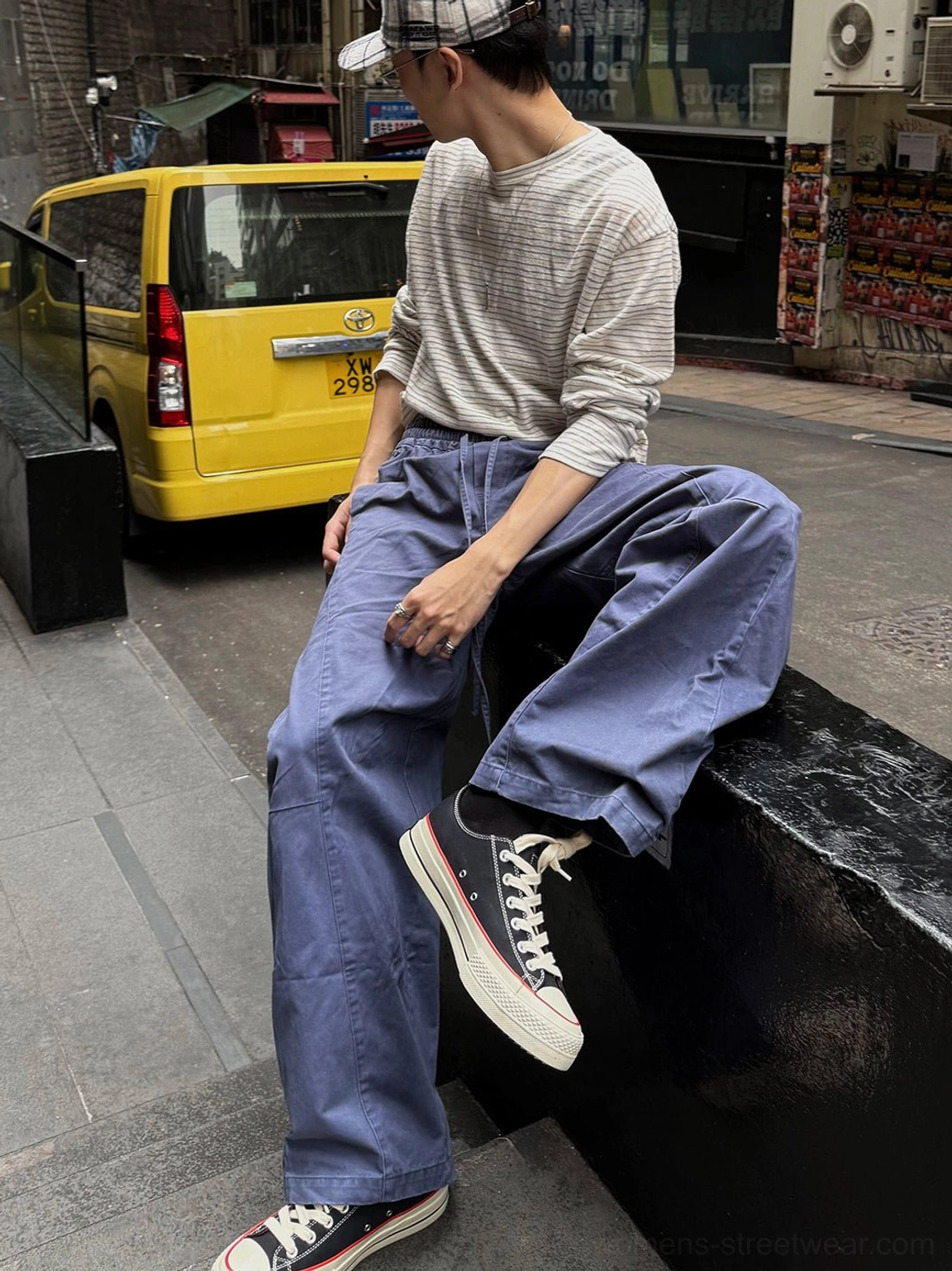 Black low-top bat print platform sneakers styled with blue cargo pants and a striped long sleeve shirt on an urban street