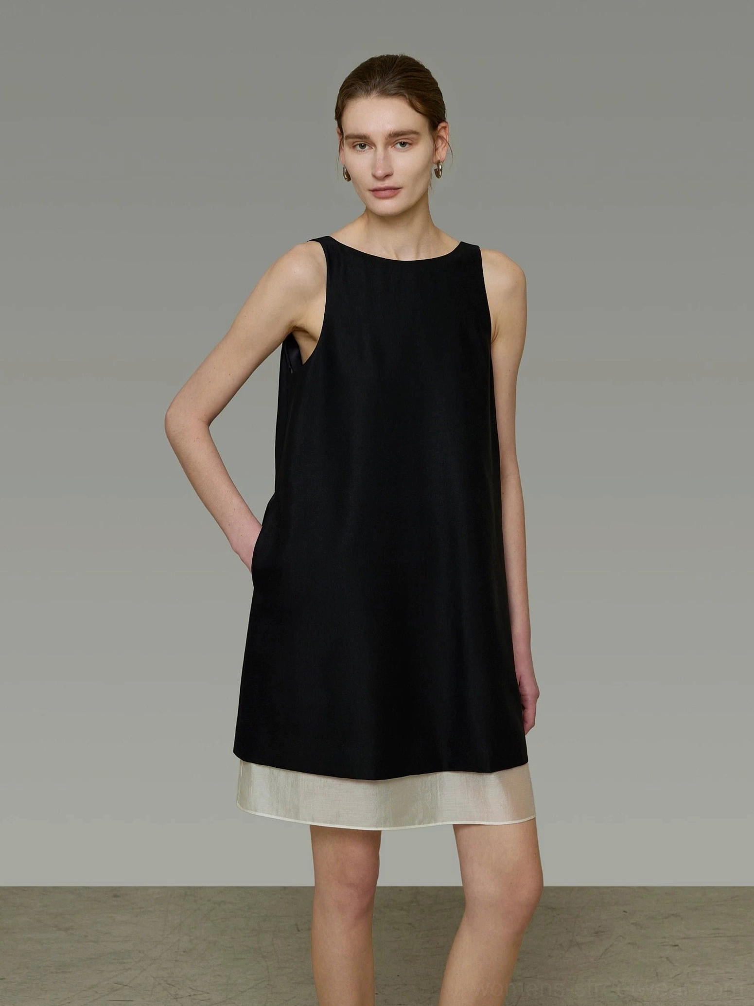 Three-quarter view of a sleeveless black color-block shift dress with ivory beige layered hem and minimalist Korean-inspired styling