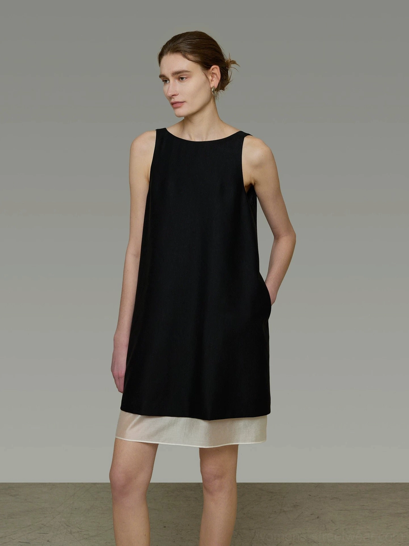 Side view of a relaxed black and beige V-back shift dress showing hidden side pockets, loose movement, and contemporary streetwear proportions