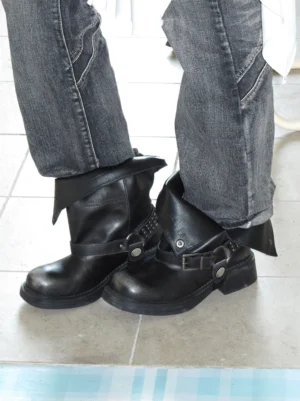 Black leather biker ankle boots styled with dark wash denim and visible triple buckle hardware