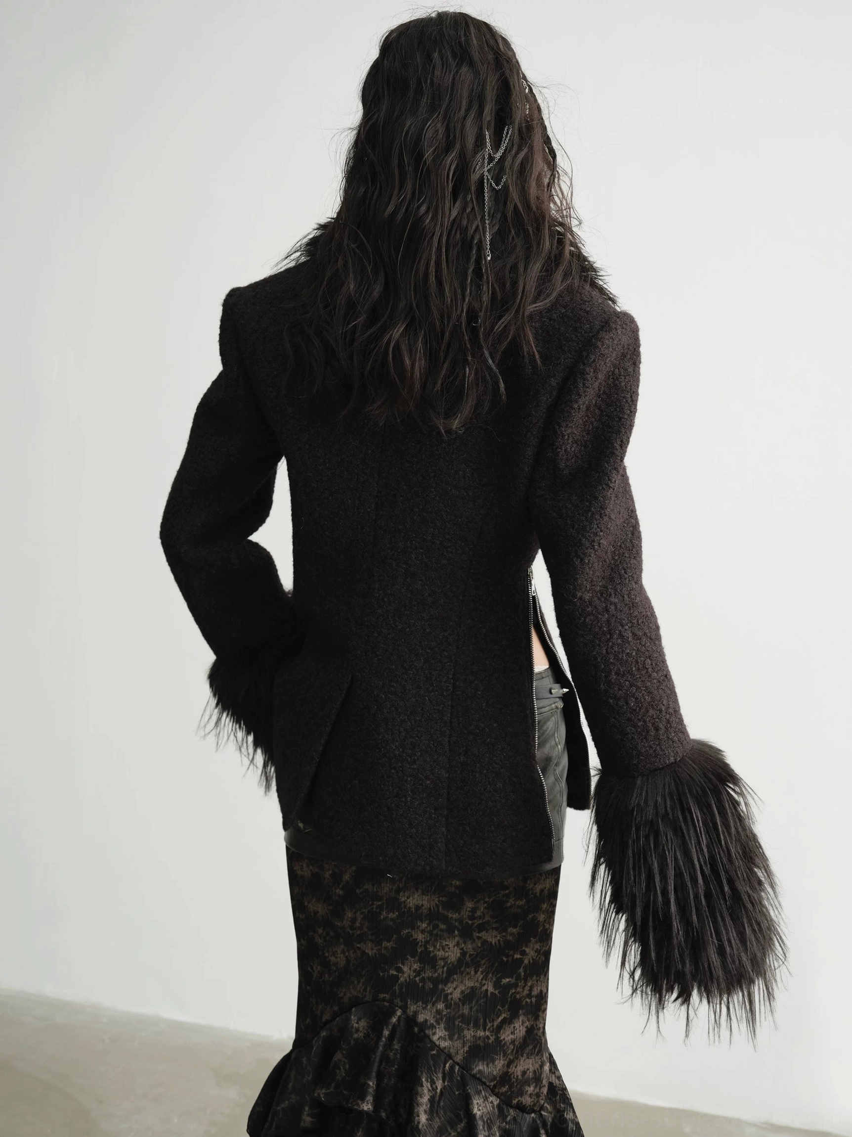 Back view of a structured black boucle-style faux fur cuff coat showing the tailored fit back hem slit and dramatic sleeve trims