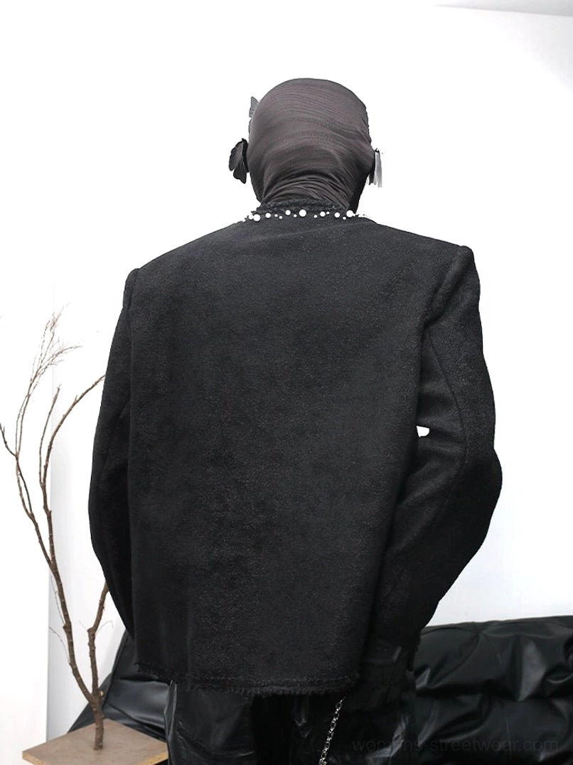 Back view of a black bouclé wool-blend streetwear jacket featuring pearl embellishments at the neckline, padded shoulders, structured silhouette, textured fabric, and raw frayed hem
