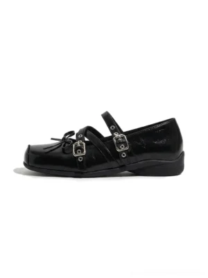 Black double-strap bow Mary Jane flats with square toe, glossy textured upper, silver buckle straps, and subtly lifted platform sole shown in a front three-quarter product view