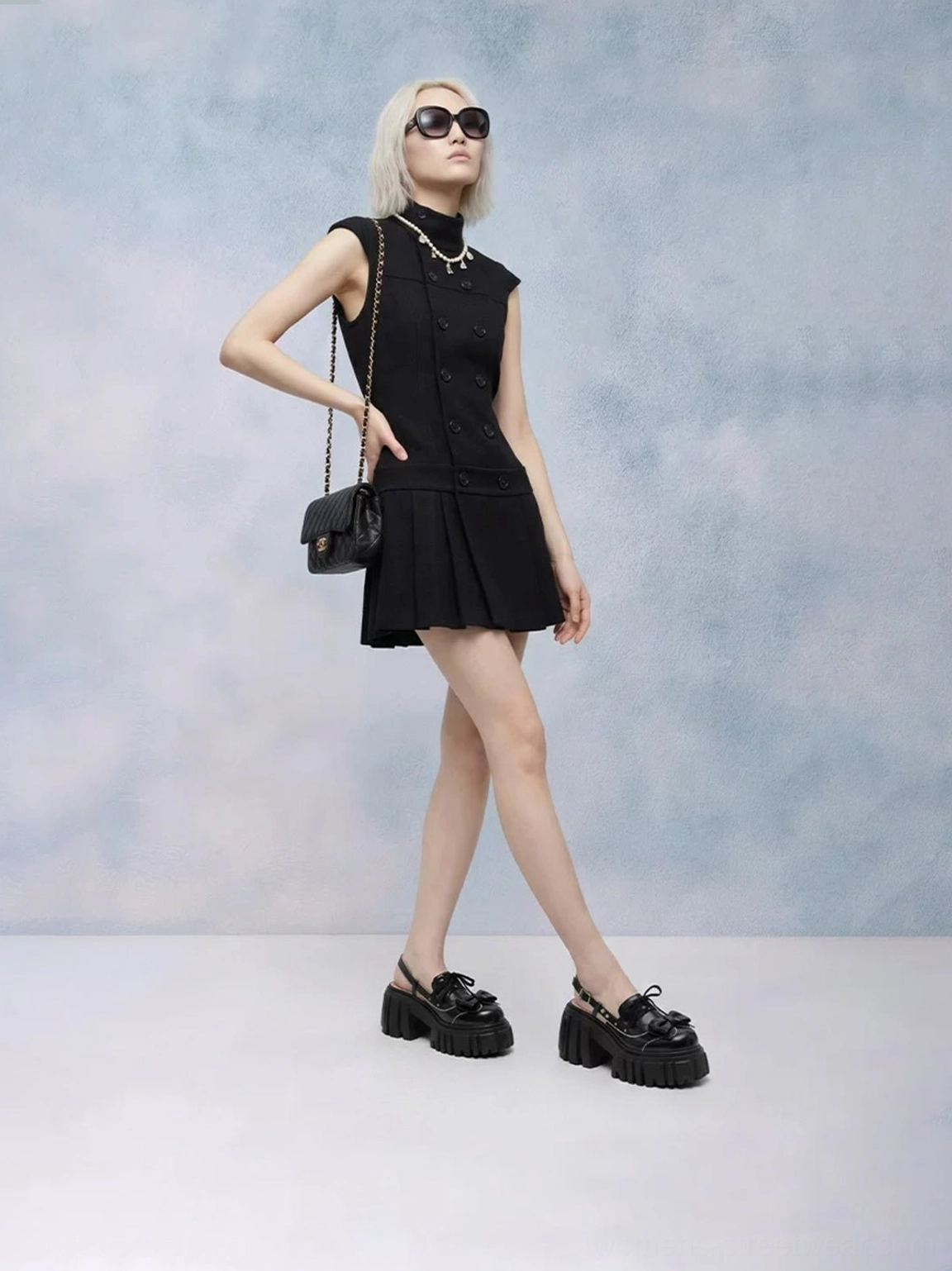 Model wearing black bow-front chunky platform Mary Jane sandals with sunglasses and a black Y2K mini dress back side view