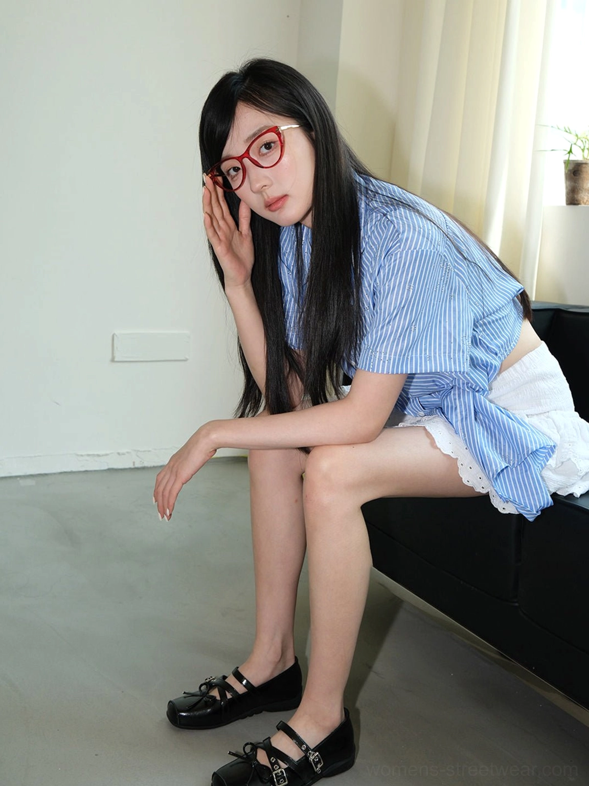 Black bow Mary Jane flats shown from the side on a seated model, highlighting the adjustable double straps, decorative bow, and lifted rubber sole