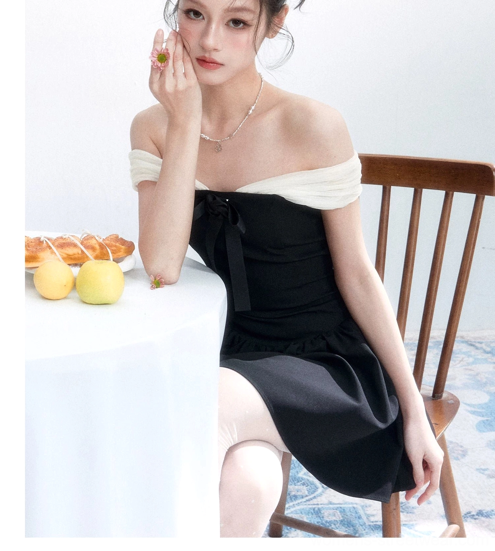 Close-up view of the black fitted bodice, front bow, and light mesh off-shoulder neckline styled with delicate jewelry