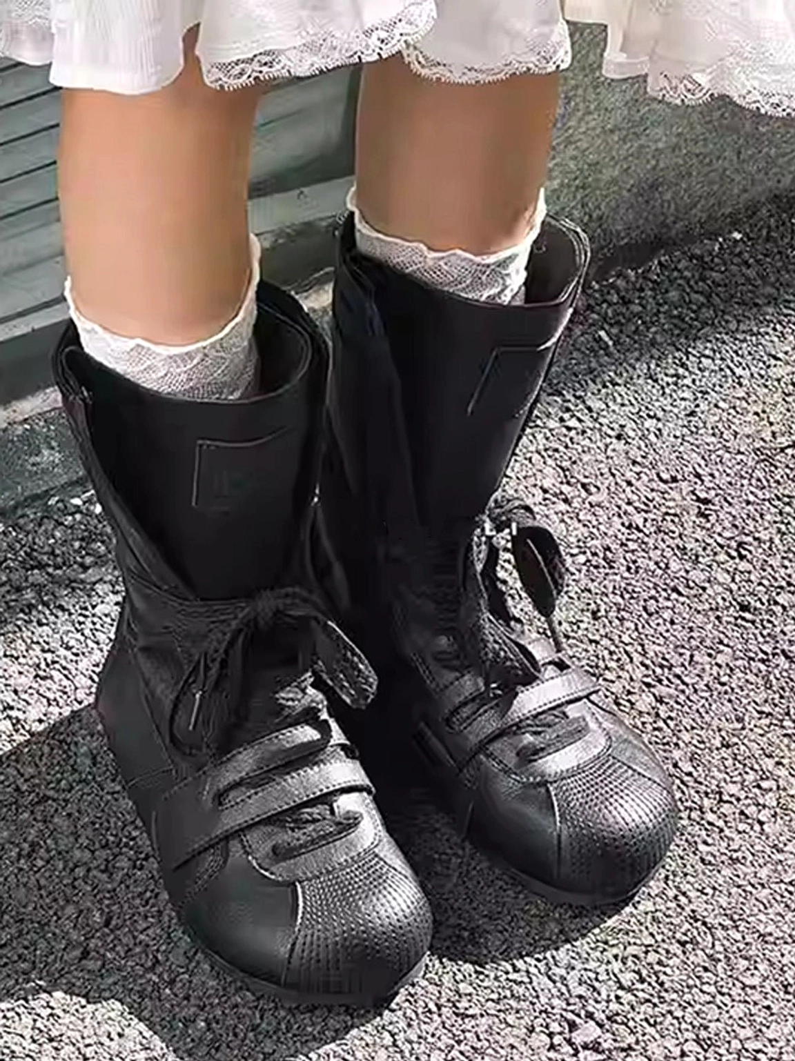 Front three-quarter view of black boxing-inspired platform boots with structured shafts and layered lacing styled with a white ruffled dress
