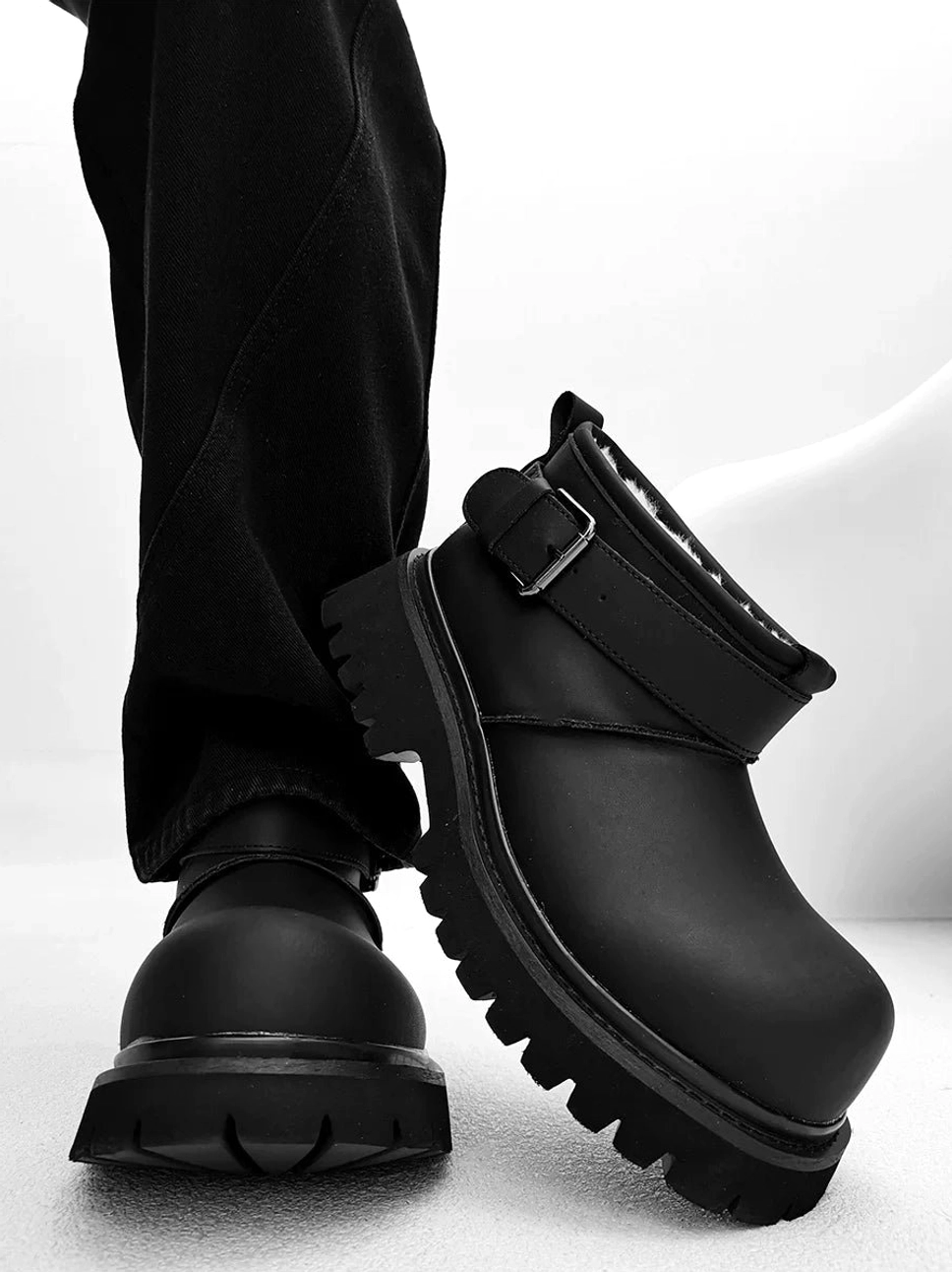 Back-side on-foot view of black buckle ankle boots with a chunky black platform outsole