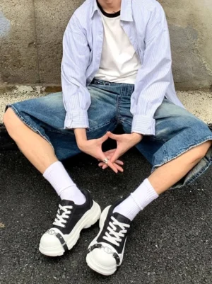 Streetwear model wearing black buckle platform canvas sneakers with white socks, baggy denim shorts, striped shirt, and casual urban styling