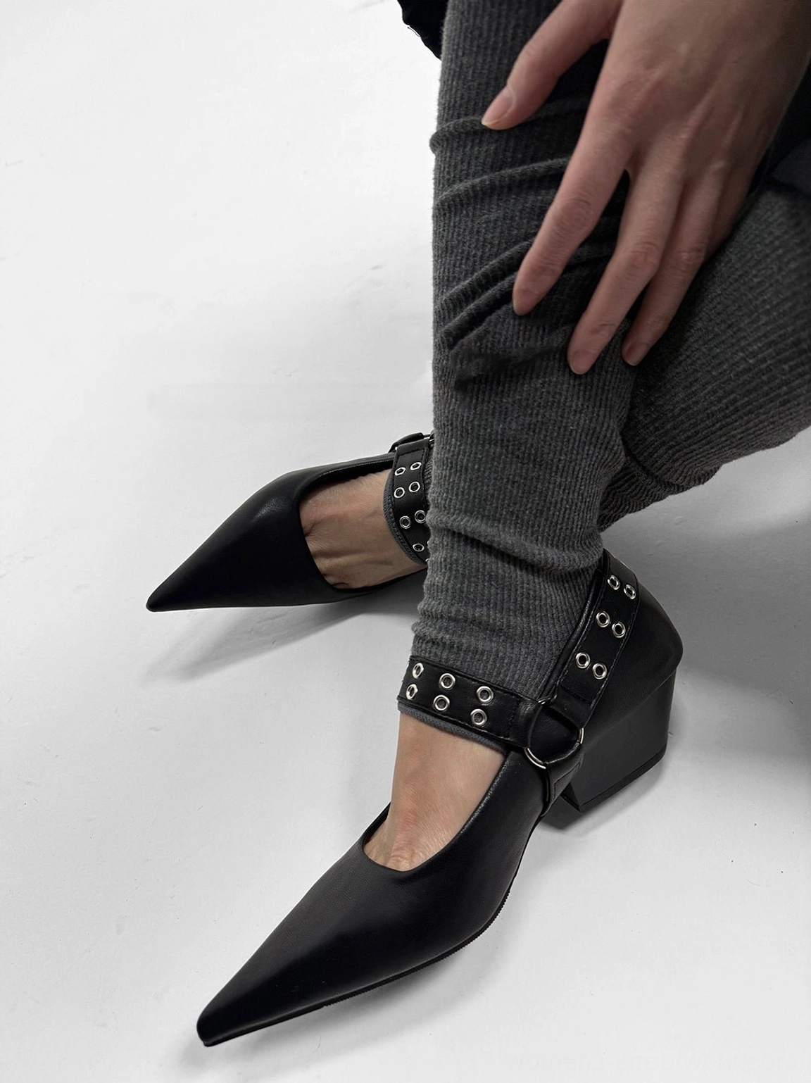 Black buckle-strap Mary Jane pump worn from a low angle with pointed toe, metal eyelets, and adjustable ankle buckle