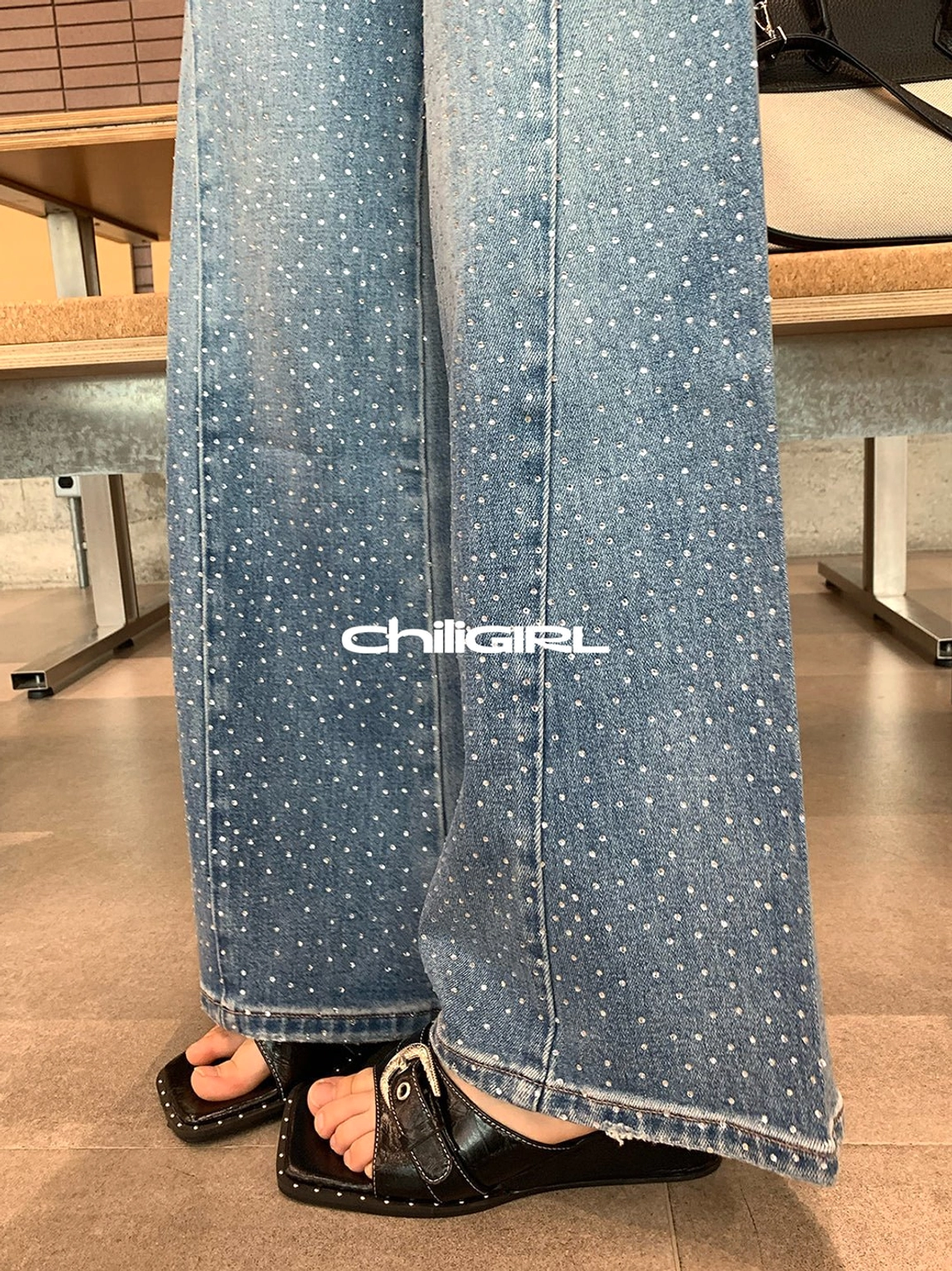 Close-up of black buckle wedge sandals peeking from beneath wide-leg denim with detailed studded sole