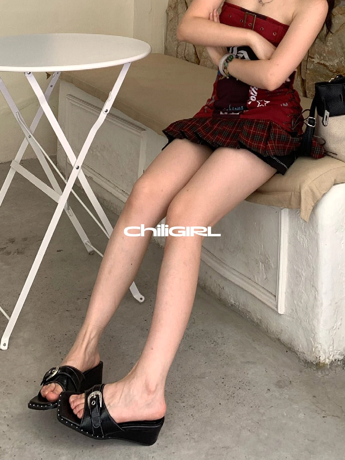 Black low-wedge slide sandals with buckle strap shown in a casual outdoor bench outfit