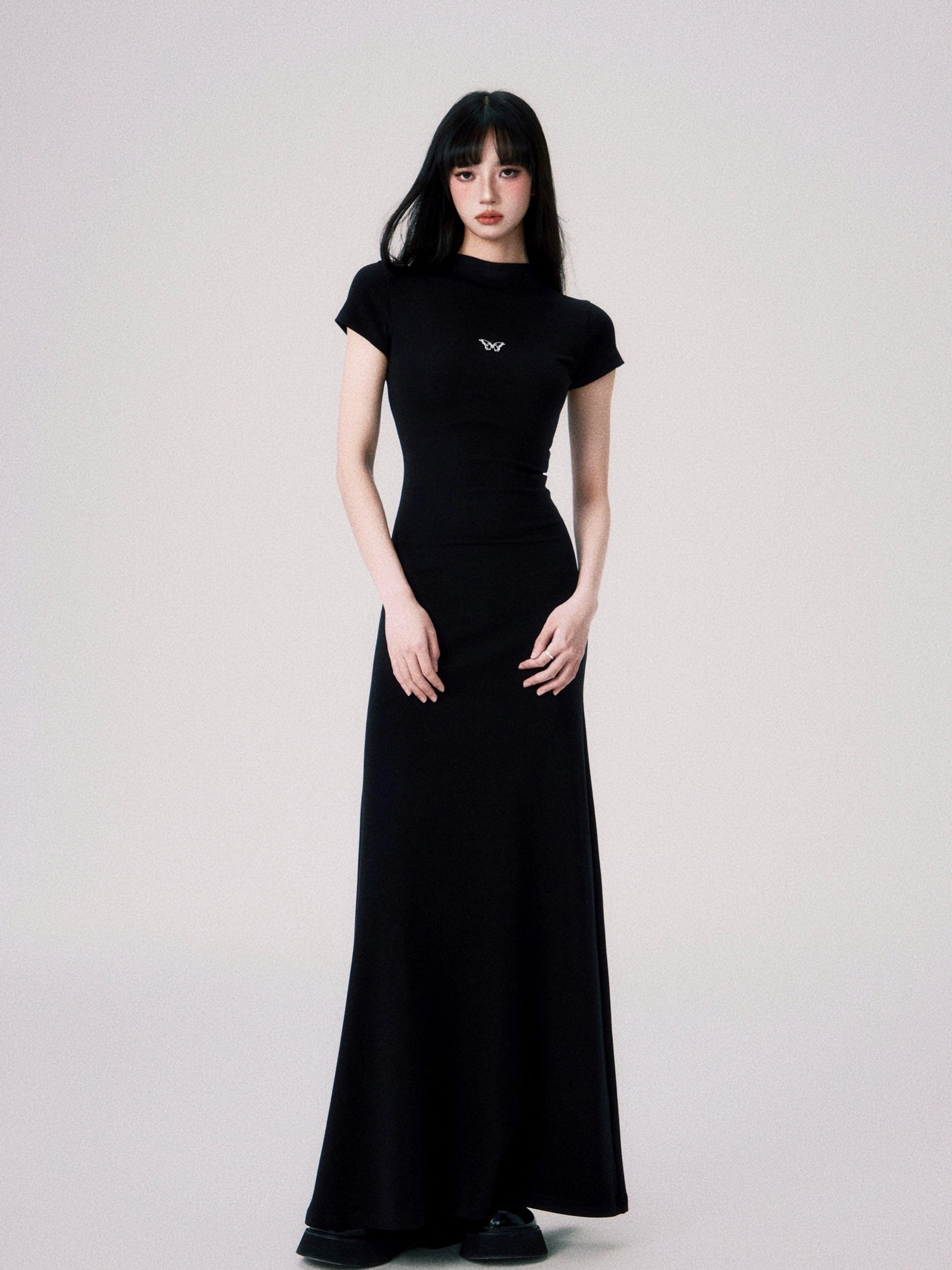Black butterfly emblem fitted maxi dress shown from the front with mock neck short sleeves and a floor length fishtail hem