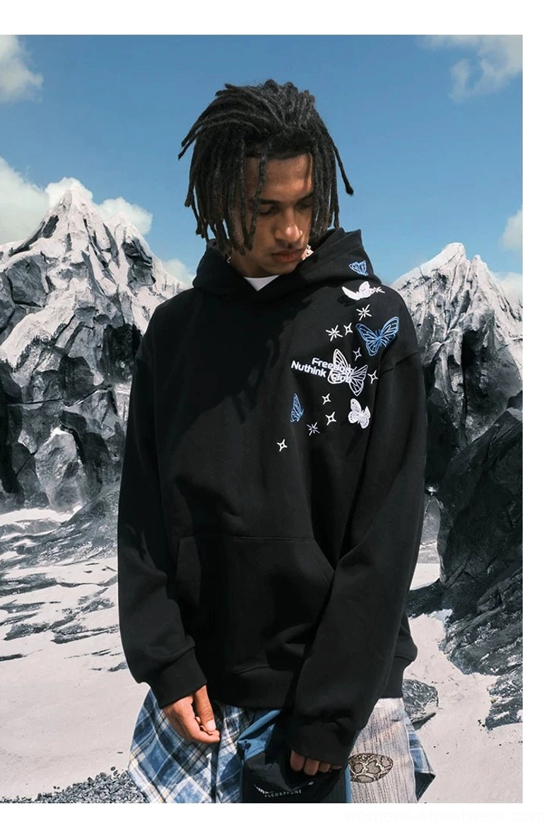 Side front view of a Black butterfly embroidered oversized hoodie styled with plaid pants in a snowy mountain setting