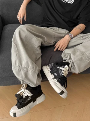 Male model wearing black distressed canvas platform sneakers with an oversized black t shirt and loose gray cargo pants