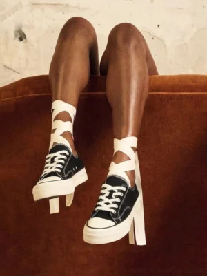 Female model wearing black canvas platform sneakers with white laces and ribbon cross-strap socks in indoor streetwear styling
