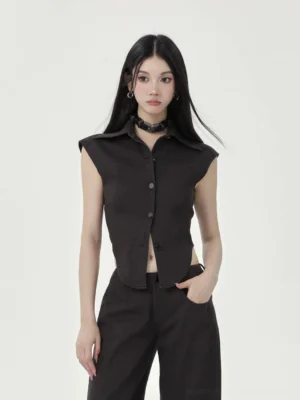 Black cap sleeve cropped button-up top styled with wide-leg trousers in a front-facing minimalist studio streetwear look