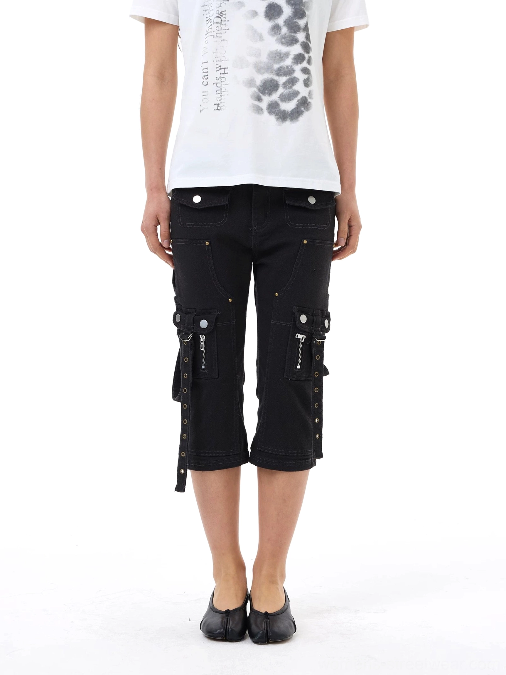 Detailed front view of black denim cargo capri jeans showing metal button waist, dual side zipper pockets, strap details, and rivet accents