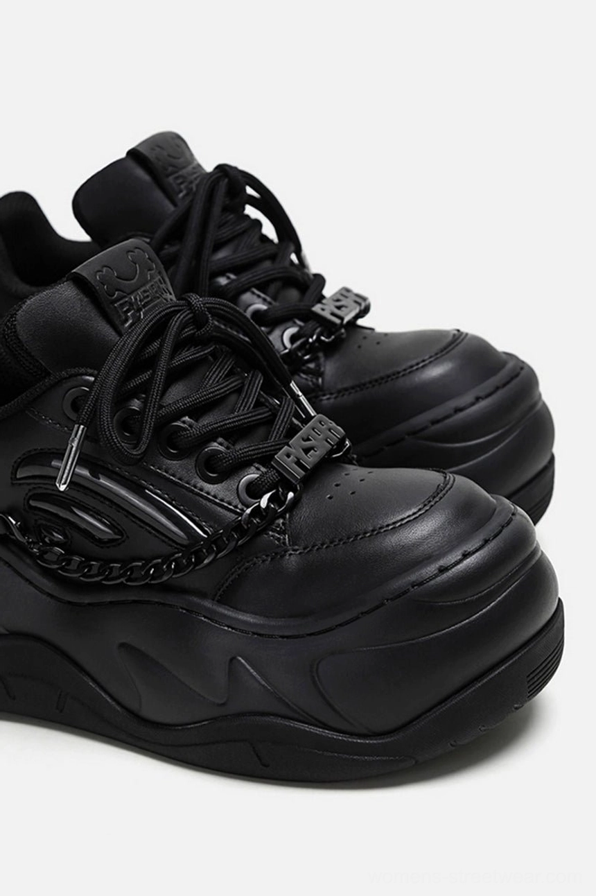Close-up overhead view of black chain platform sneakers with metal lace hardware, detailed vamp chains, and raised thick rubber sole