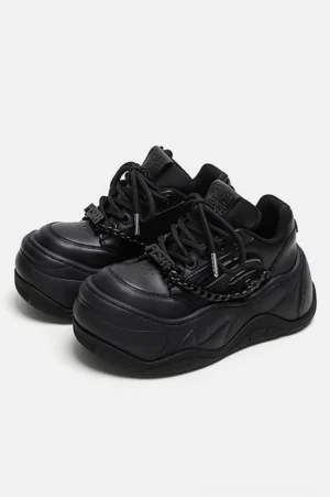 Front three-quarter view of matching black platform sneakers with lace-up closure, silver chain vamp trim, and bold chunky wave soles