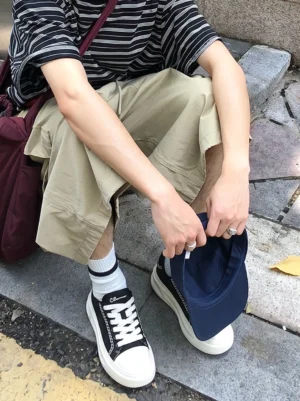 Black chain-trim platform sneakers styled with a striped tee and khaki cargo shorts on outdoor stone steps for a casual streetwear outfit