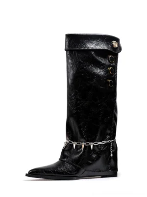 Front view of black chain-trim pointed-toe knee-high riding boots with crinkled textured finish, layered spike chain ankle hardware, fold-over shaft, and low wedge heel