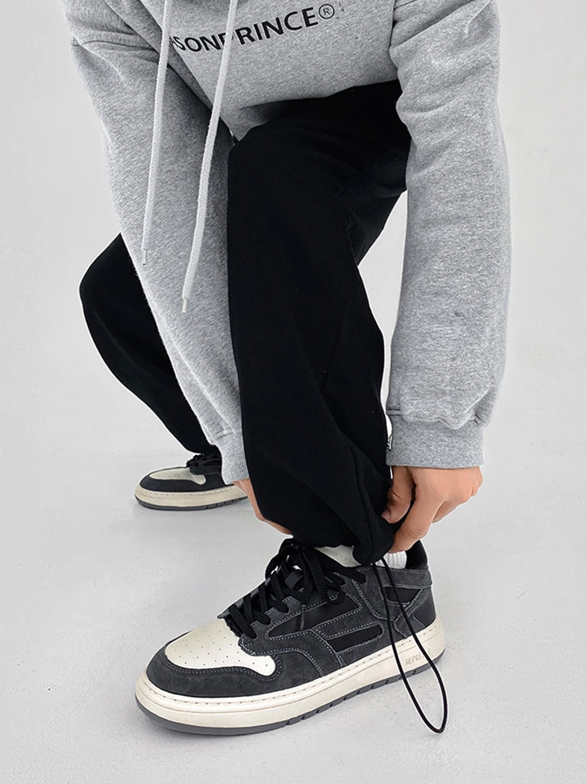 Model adjusting black joggers while wearing black and charcoal suede-look low-top casual streetwear sneakers