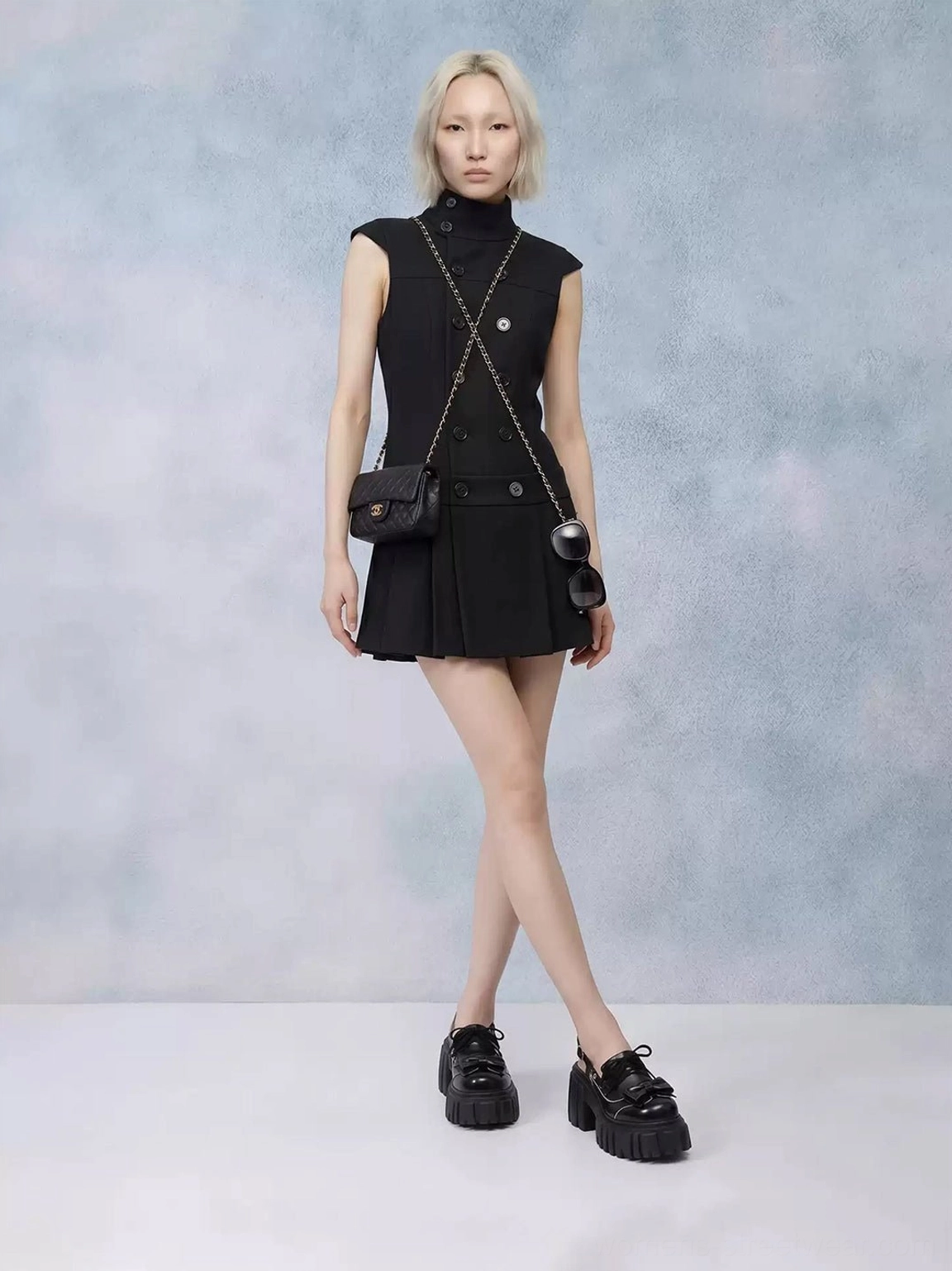 Side profile of model styling black chunky bow Mary Jane sandals with a sleeveless black pleated dress and crossbody bag