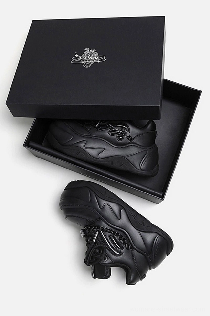 Top-down retail packaging view of black chunky chain sneakers with one shoe in an open box and one shoe displayed outside