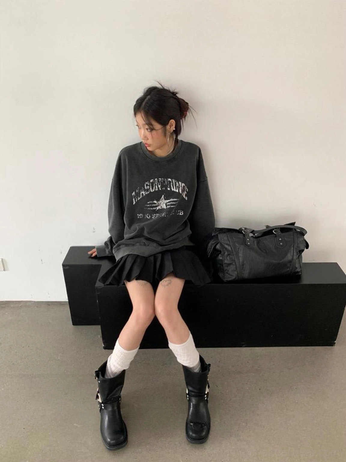 Black chunky heel Western boots with double harness buckles styled with a printed sweatshirt, pleated skirt, and leather bag