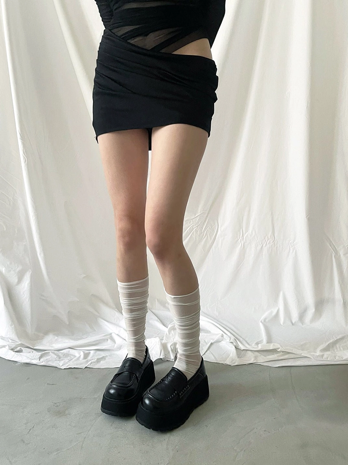 Black chunky platform loafers worn with a mini skirt and striped knee-high socks for a preppy streetwear look