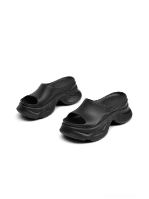 Pair of black chunky platform slide sandals in front three-quarter view with exaggerated open toe wedge soles
