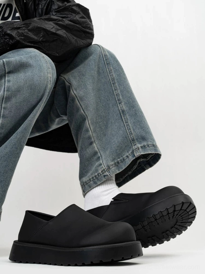Black chunky platform slip-on clogs with open heel and rugged lug outsole worn with white socks and jeans