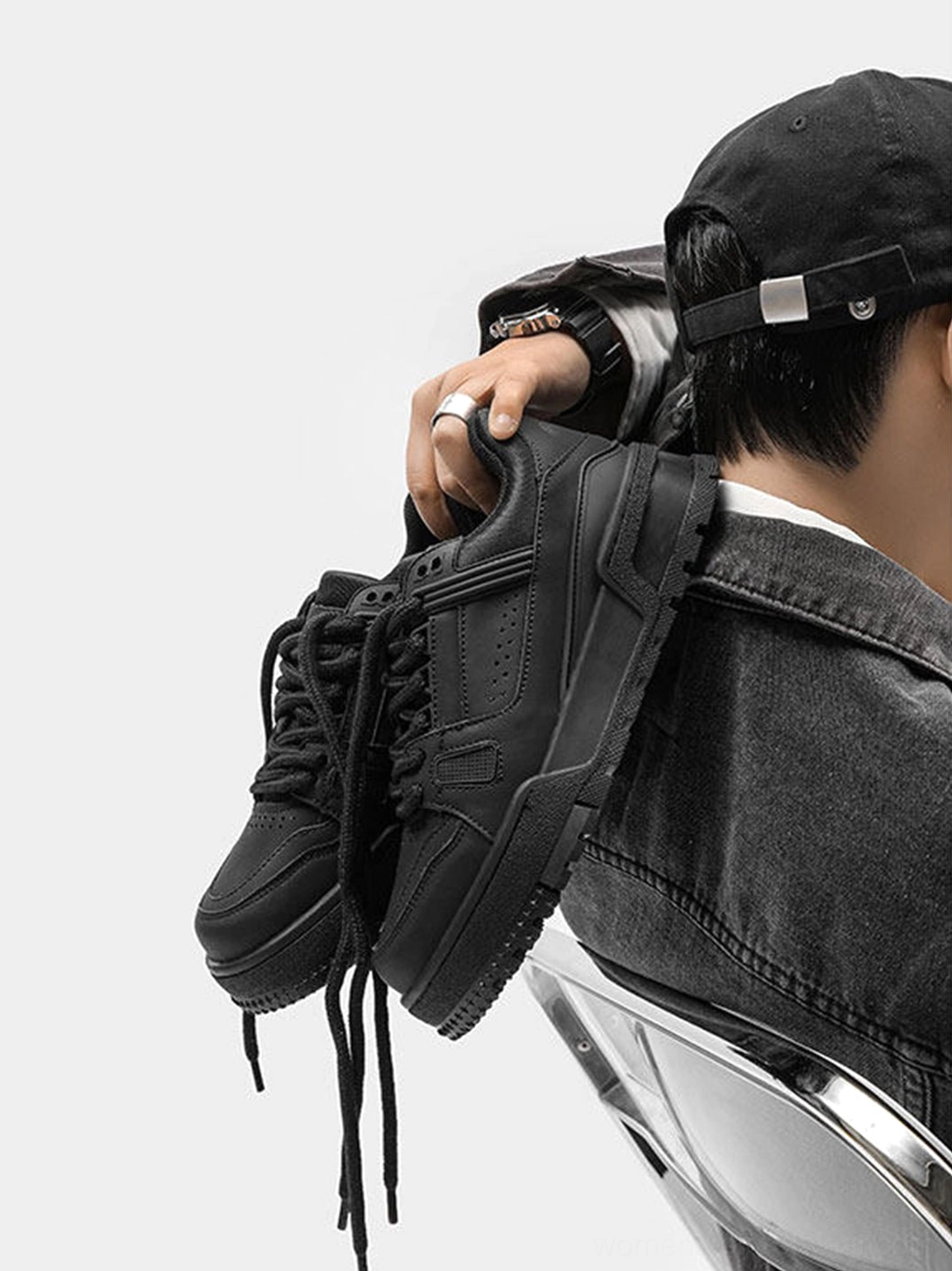 Black chunky platform sneaker held in hand showing the heel tab hanging laces side panel detailing and thick rounded sole