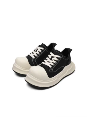 Front flat lay view of black chunky platform sneakers with oversized white round toe caps, off-white laces, contrast stitching, and thick two-tone soles