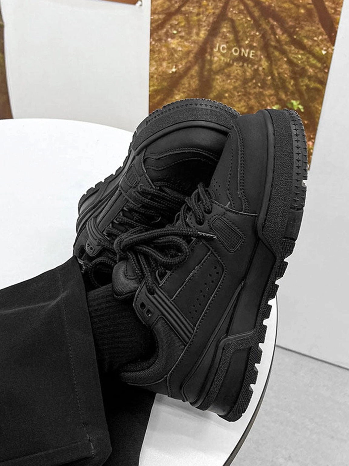 Overhead close-up of black chunky platform sneakers on a white surface showing upper stitching perforated side panels and rugged outsole