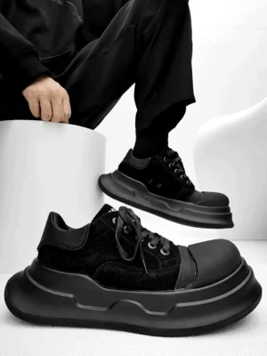 Black chunky platform sneakers shown in a flat lay and partial on-foot view with layered suede finish panels, rounded wave sole, reinforced toe, and all-black streetwear styling