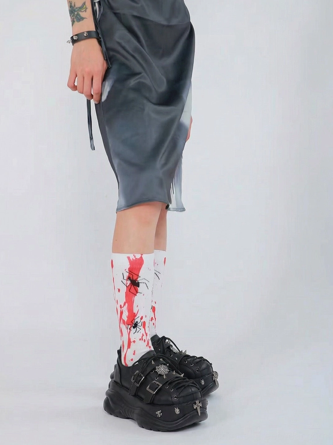 Side view of black chunky punk platform sneakers paired with a gray mini skirt and printed socks, featuring double buckles and metal studs