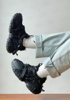 Black chunky racing sneakers worn with light blue jeans and white ankle socks, showing lace-up fastening, adjustable straps, and platform sole