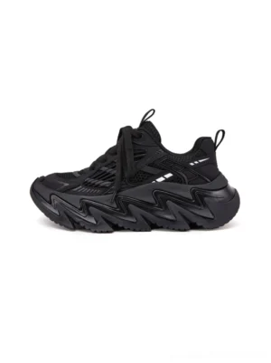Black chunky runner sneakers in a left-side flat lay view with layered microfiber panels, lace-up front, mesh-style upper, heel pull tab, and bold zigzag rubber outsole
