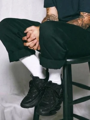 Black chunky streetwear runner sneakers styled with dark green trousers and white socks, showing the technical sole and urban silhouette