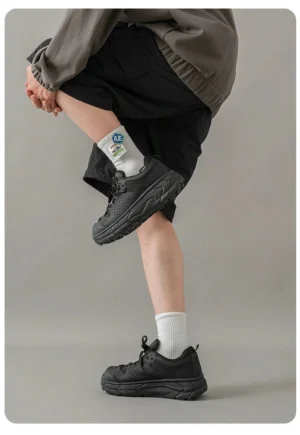 Black chunky utility hiking trainers worn with a gray hoodie black shorts and printed crew socks, showing the breathable perforated upper and thick anti-slip trail sole from a rear low angle