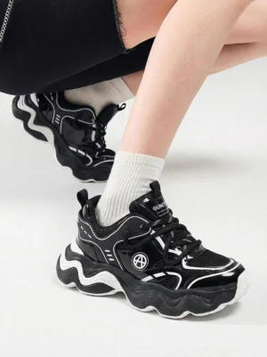 Black chunky wave sole dad sneakers worn with white crew socks and cropped black denim, showing breathable mesh panels and wavy rubber-style outsole