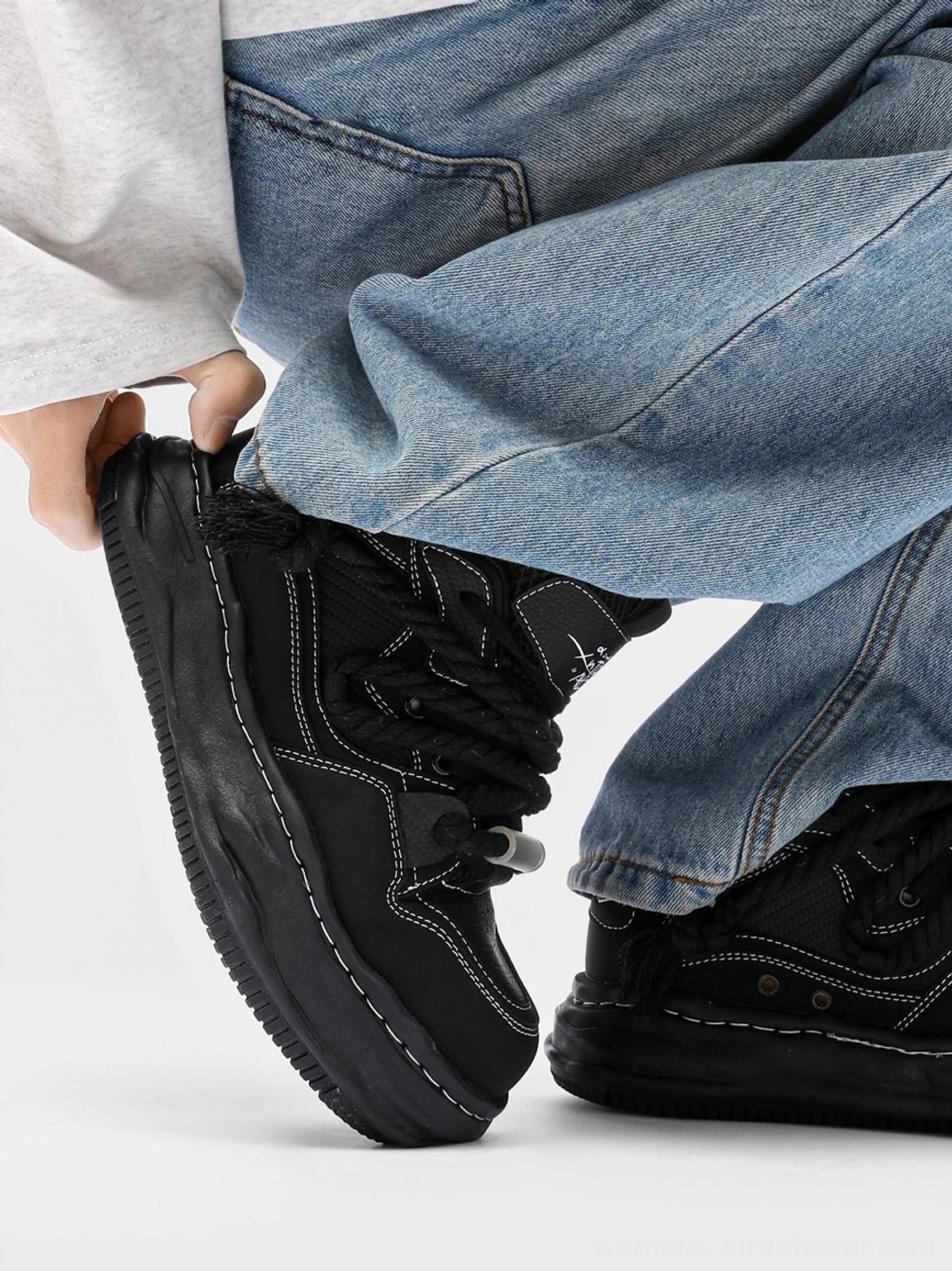 Black chunky wavy platform sneakers worn with baggy blue denim for a contemporary unisex streetwear look