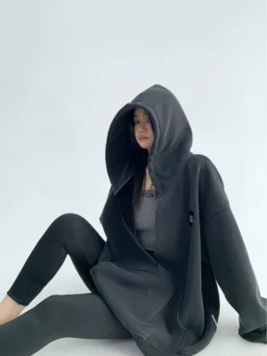 Black cocoon oversized hoodie side sitting view showing plush fleece texture large hood and relaxed streetwear fit