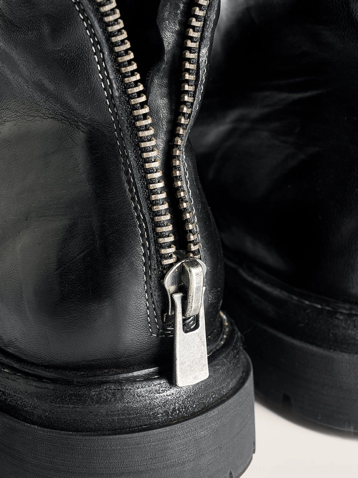 Macro close-up of the black combat boot rear zipper showing silver metal zipper teeth, pull tab, stitched heel leather, and interior lining